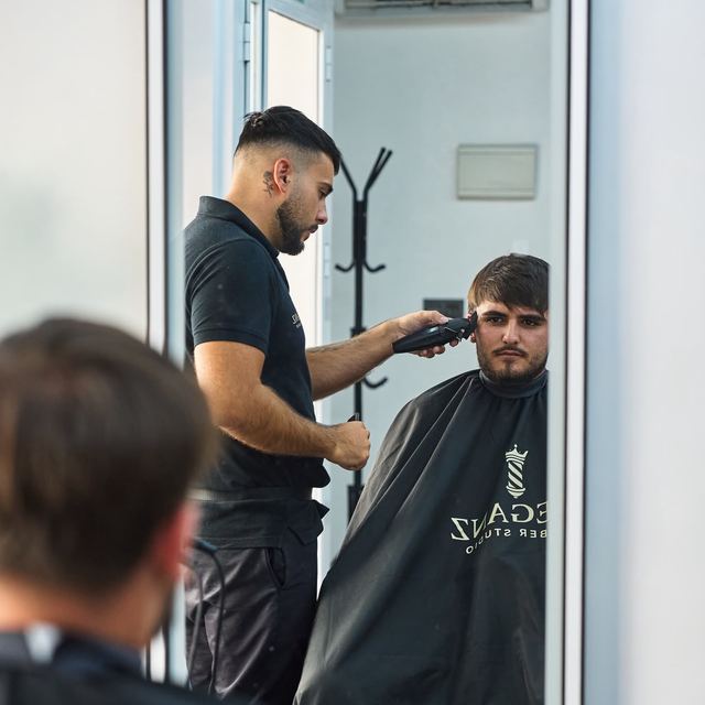 Rafa cortando el pelo a un cliente, reflejado en el espejo del estudio