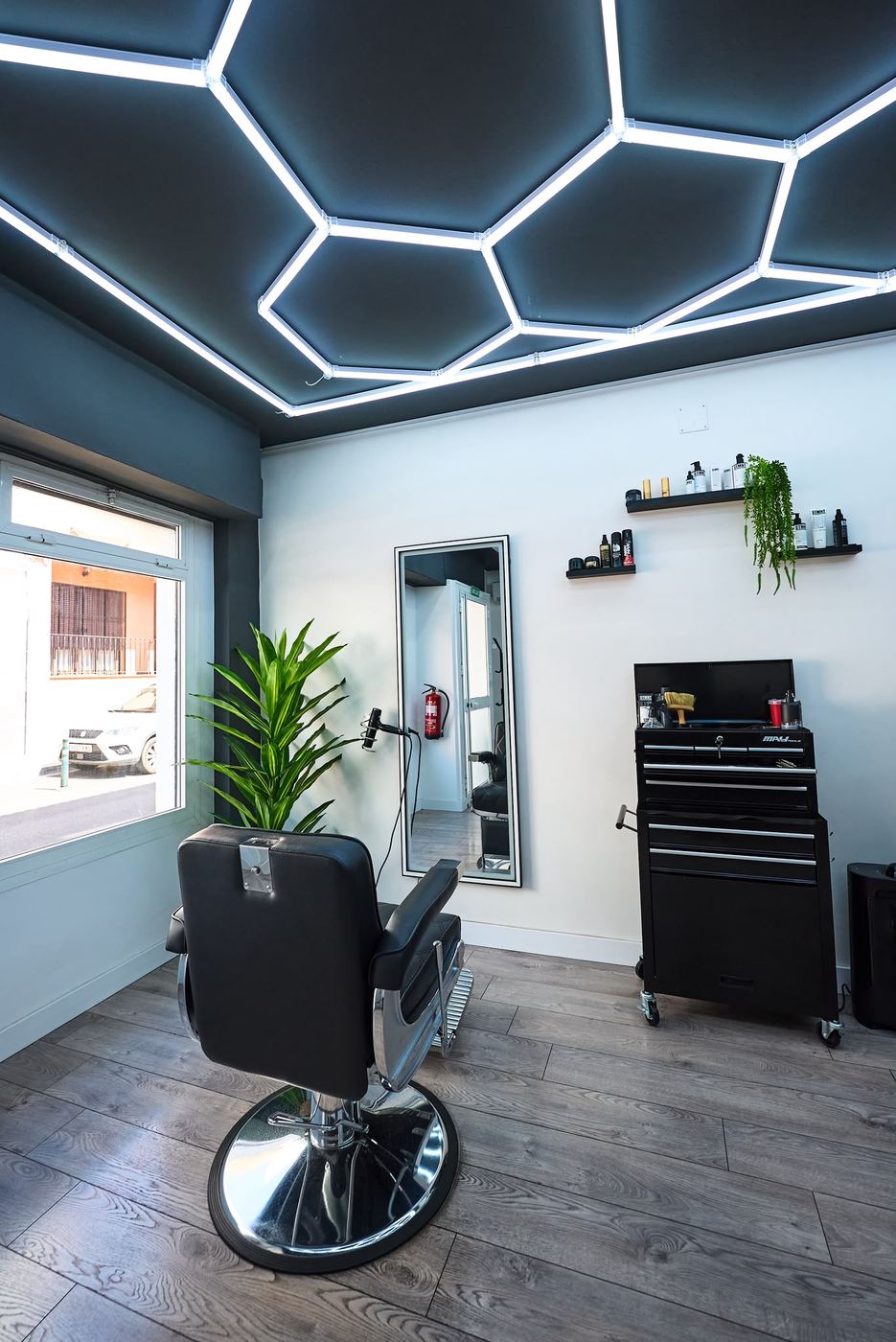 Sillón de barbero bajo el techo de luz hexagonal, con espejo y estanterías de producto